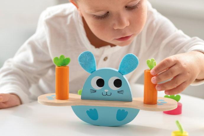 Criança a brincar com balança de madeira coelho e cenouras da marca Goula.